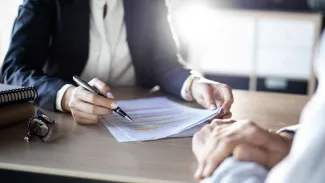 A businesswoman holding a pen over a document in a meeting. 